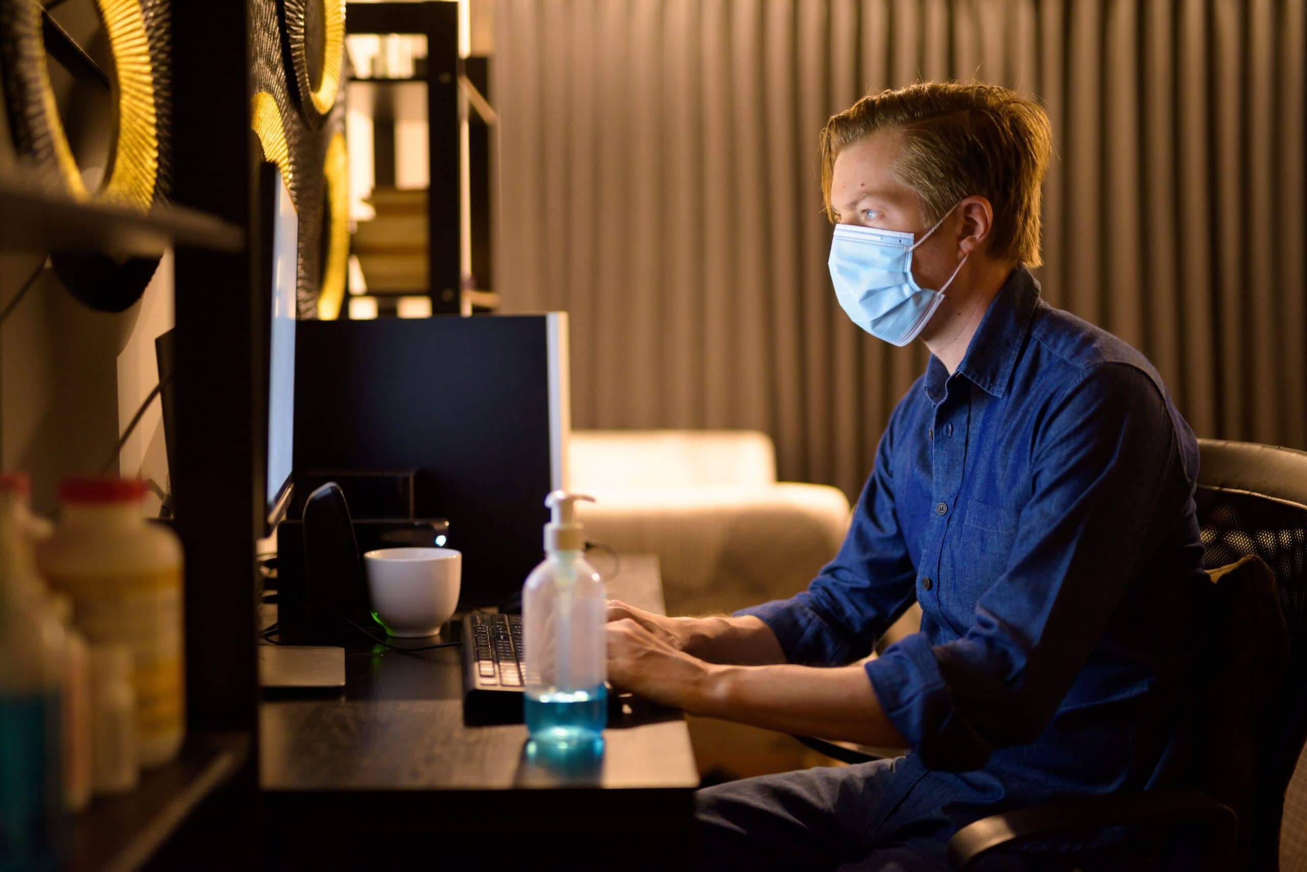 Young businessman with mask for protection from corona virus outbreak working from home during quarantine